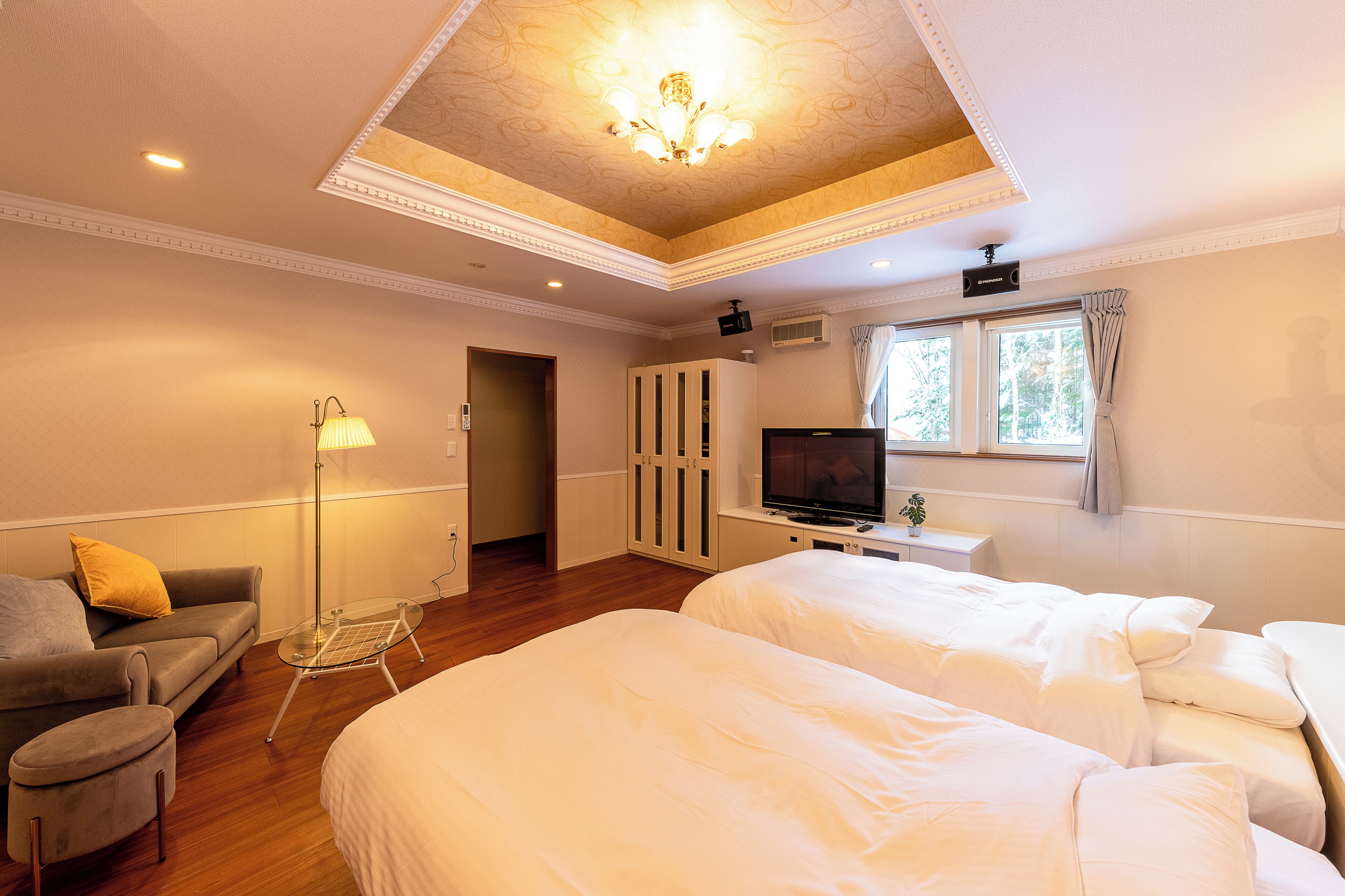 A hotel room with two beds, a TV, a lamp, a sofa, and a window with curtains.