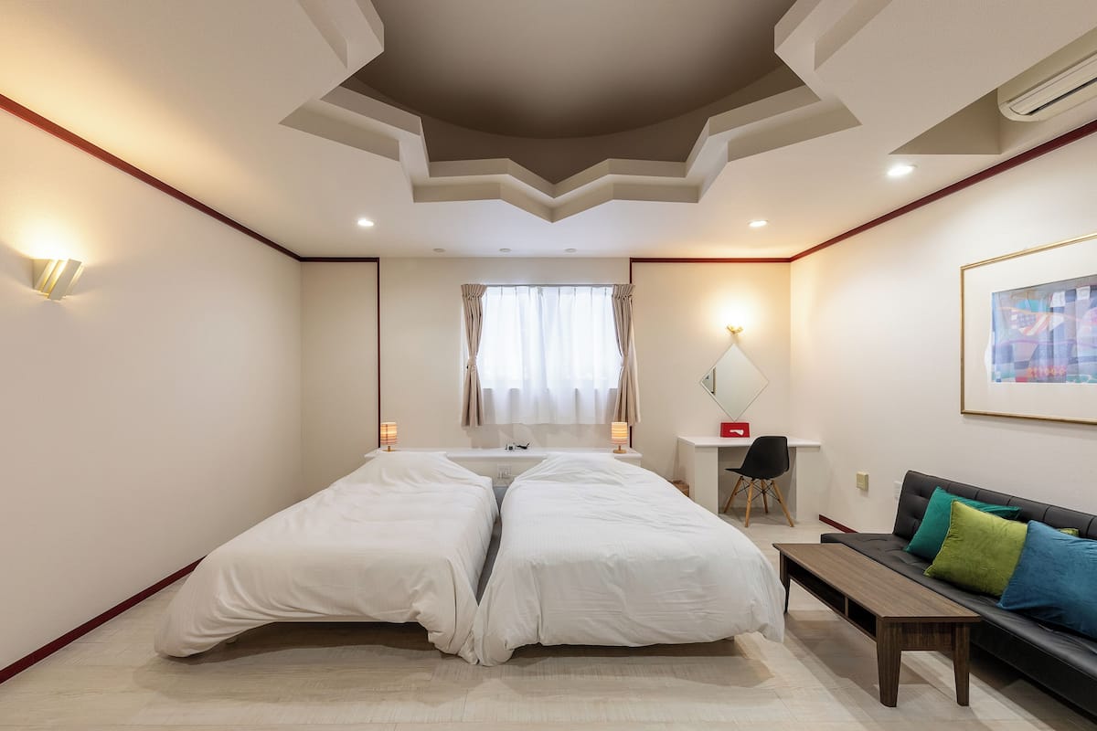 Een hotelkamer met een tweepersoonsbed, een bureau met stoel, een bank en een groot raam met gordijnen.