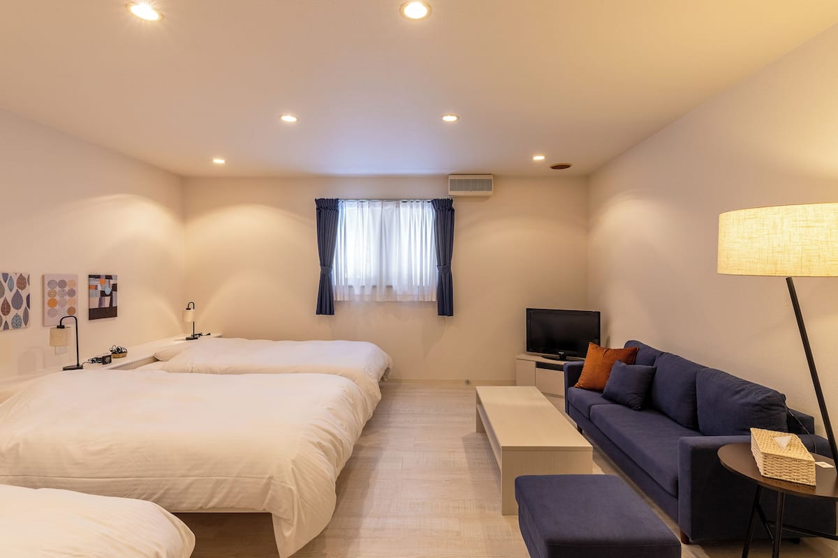 Een hotelkamer met twee bedden, een slaapbank, een televisie en een lamp.