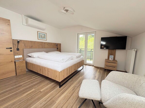 A bedroom with a wooden bed, a TV, a chair, and a balcony with a view.