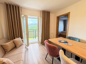 A room with a sofa, a wooden table, a chair, and a balcony with curtains.
