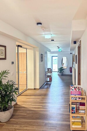 A hallway with wooden flooring, a potted plant, a bookshelf, and a door leading to another room.