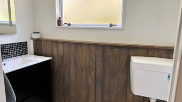 A bathroom with a white sink, wooden paneling, a toilet, and a window with blinds.
