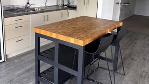 A modern kitchen with a wooden table, black chairs, and a built-in oven. - Spacious Three Bedroom Coastal Apartment in Army Bay (Whangaparāoa)