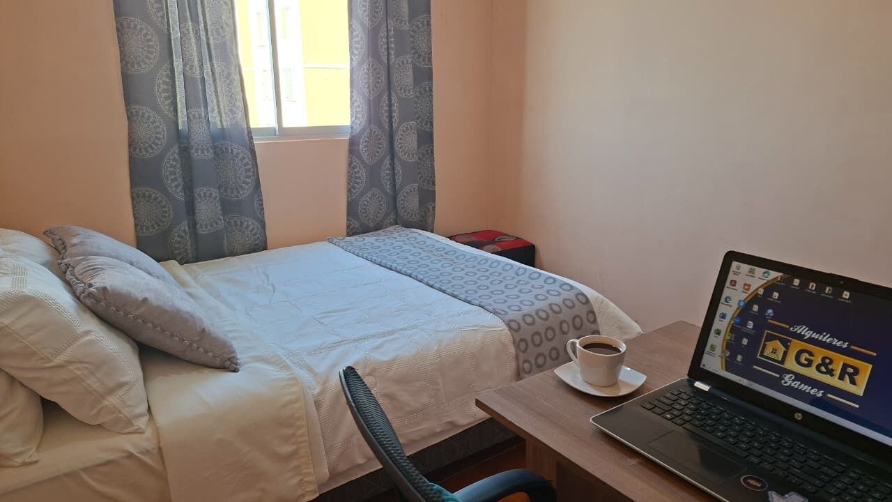 A hotel room with a bed, a laptop on a desk, and a cup of coffee.