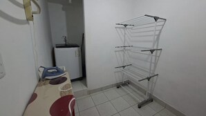 Et lille vaskerum med tørrestativ, strygejern og vaskemaskine.
