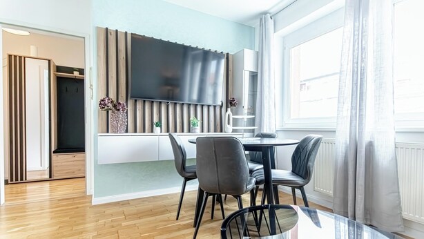 A modern kitchen with a large TV, a dining area with a glass table, and a view of the outside through a large window. - Stylish 1BR 1LR Vienna Center Homes (Vienna)