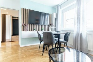 Une cuisine moderne dotée d’un grand téléviseur, d’un coin repas avec une table en verre et offrant une vue sur l’extérieur grâce à une grande fenêtre.