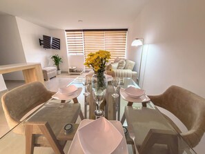 A modern dining area with a glass table, chairs, and a vase with yellow flowers. - 12th Floor City View Apt| Breeze, WiFi & Parking (Ibagué)