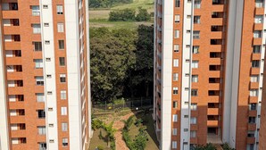 Un immeuble résidentiel de grande hauteur doté de nombreux balcons, d’une cour aménagée et offrant une vue sur un paysage lointain.