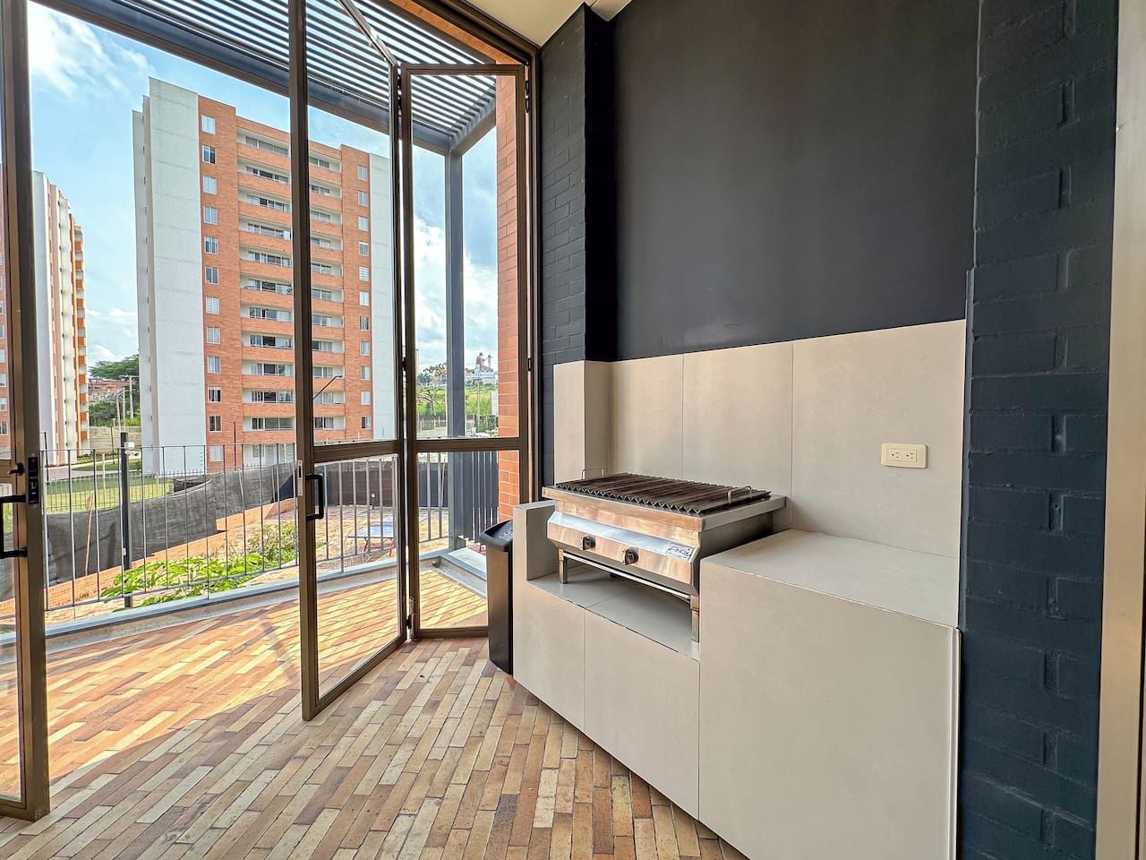 Uma varanda com churrasqueira, porta de correr de vidro e vista para edifícios altos.