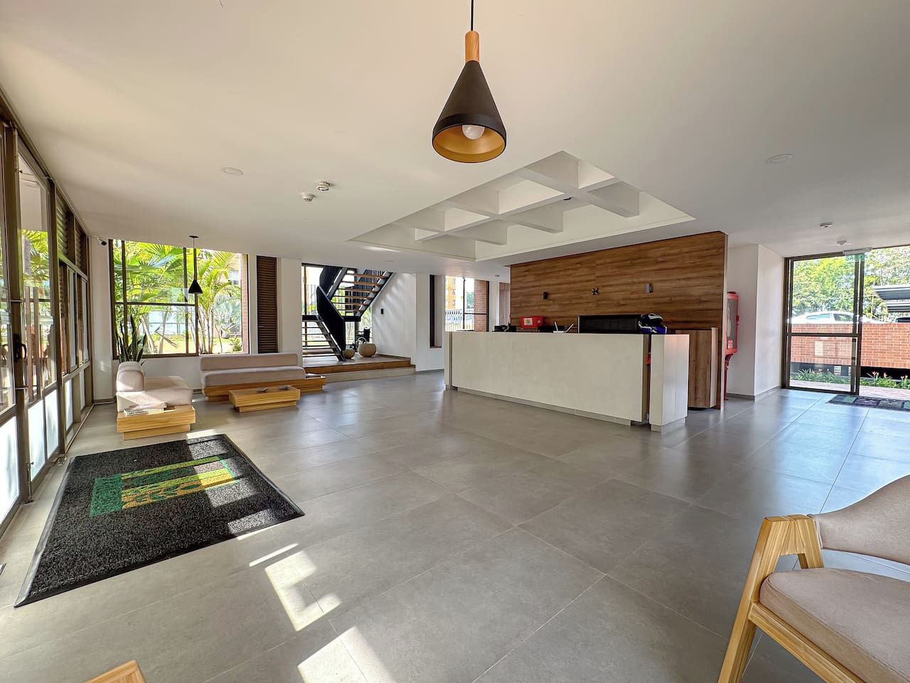 A spacious living area with a kitchen, a staircase, and large windows.