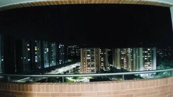 A nighttime view from a balcony with a brick wall, overlooking a cityscape with tall buildings and a road.
