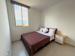 A bedroom with a bed, bedside table, and a window with blinds. - 12th Floor City View Apt| Breeze, WiFi & Parking (Ibagué)