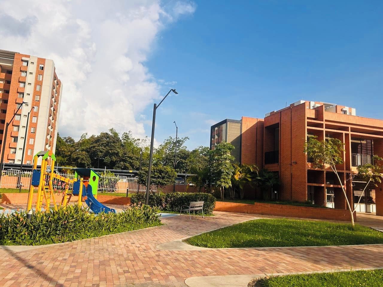 A playground with a slide and swings, surrounded by a brick pathway and greenery.