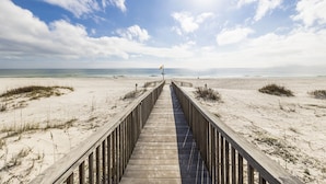A wooden boardwalk leading to a beach with a flag on a pole. - Beach Club Condos  (Gulf Shores)