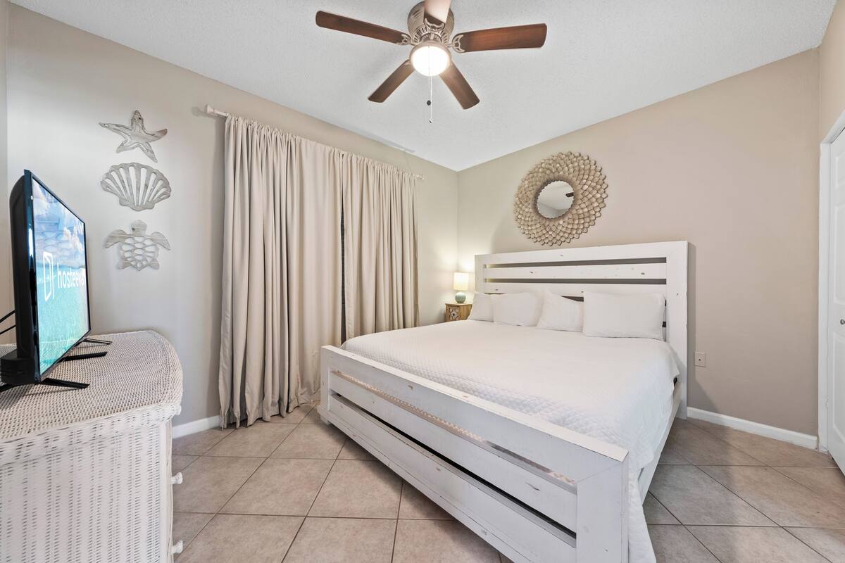 A bedroom with a bed, a ceiling fan, a television on a stand, and decorative wall art.