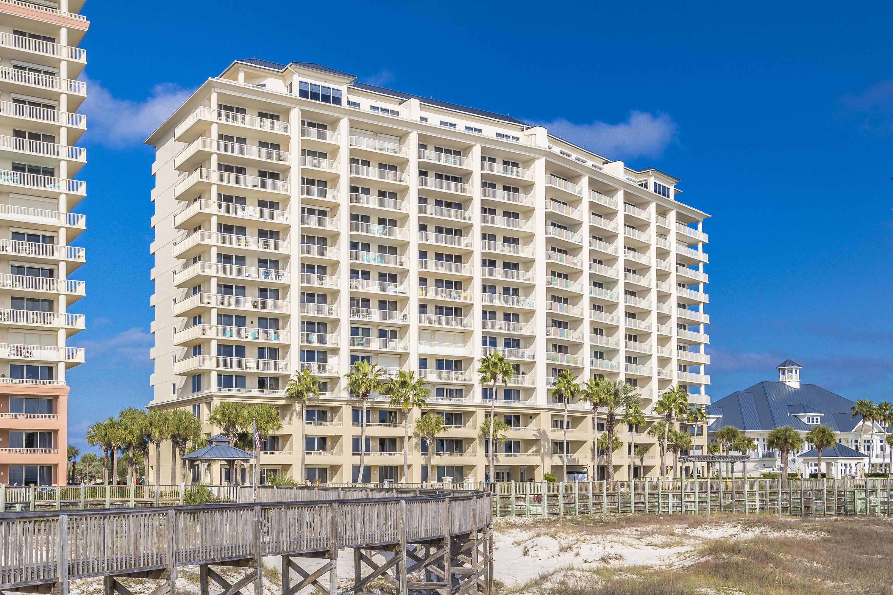 A high-rise hotel with multiple balconies, a beach view, and a wooden boardwalk.