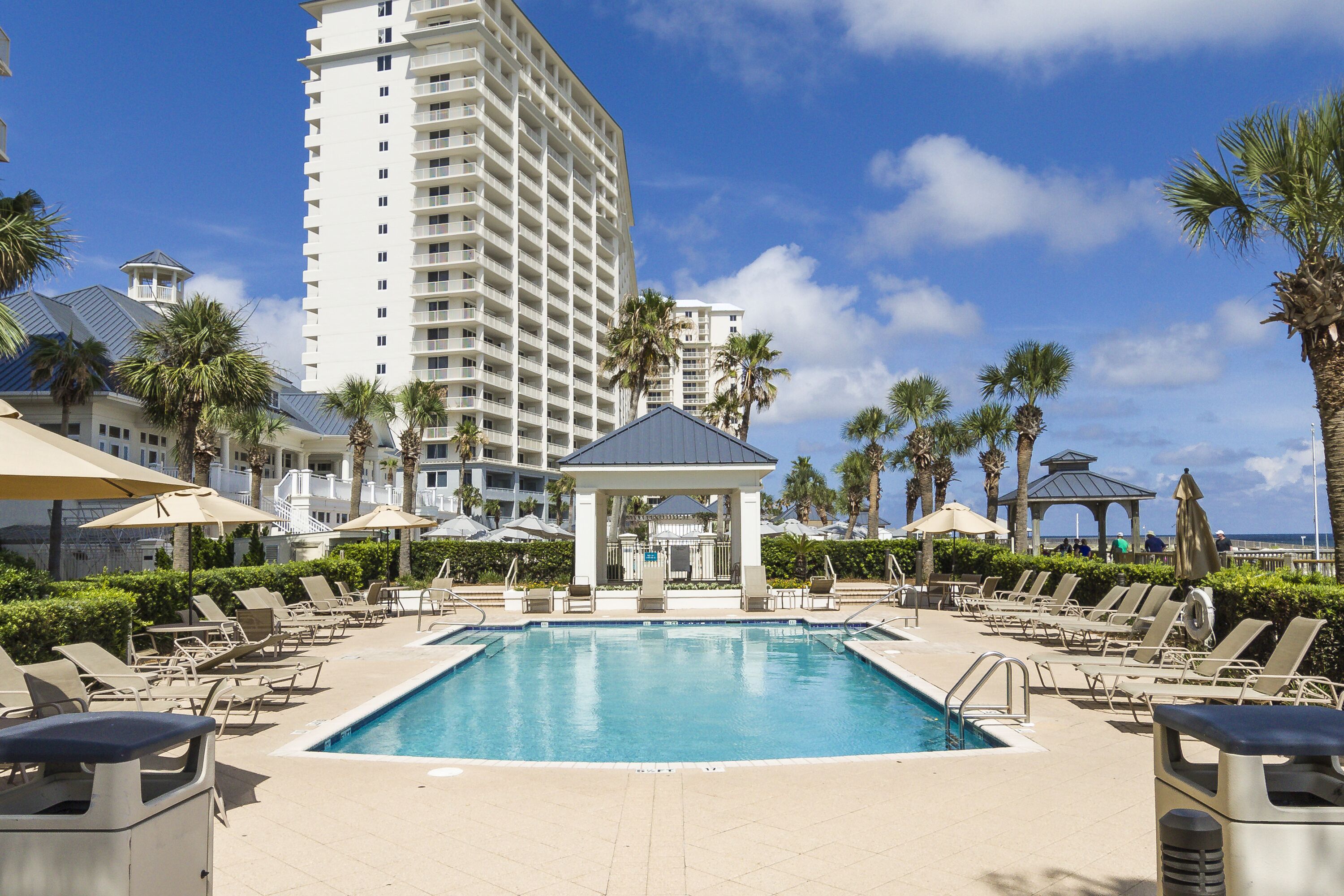 A pool area with lounge chairs, a gazebo, and a tall building in the background.