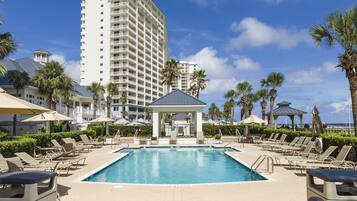 A pool area with lounge chairs, a gazebo, and a tall building in the background.