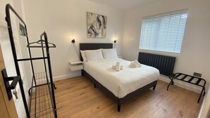 A neatly arranged bedroom with a bed, a bedside table, a radiator, a window with blinds, and a wall-mounted artwork. - Ready Stay (Birmingham)