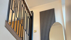A staircase with wooden steps and black metal railings, a wall-mounted light switch, and a round mirror. - Ready Stay (Birmingham)
