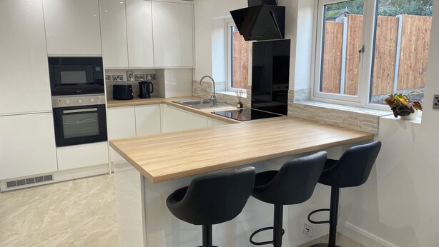 A modern kitchen with white cabinets, a wooden countertop, a built-in oven, a coffee maker, and a window with a view of a wooden fence. - Ready Stay (Birmingham)