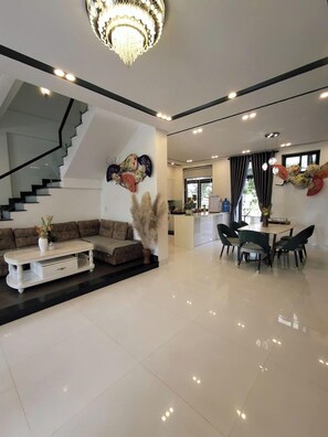 A spacious living area with a modern staircase, a dining table with chairs, and a kitchen in the background. - ConiHouse - Homestay & Villa  (Hue)
