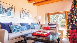 Una sala de estar con dos sofás, una mesa de centro con libros, un árbol de Navidad y pinturas de mariposas en la pared.