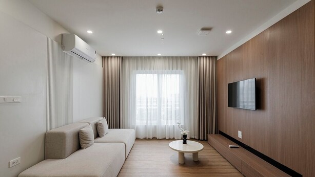 Un salon moderne avec un canapé, une table basse, un téléviseur à écran plat fixé au mur et une grande fenêtre avec des rideaux.