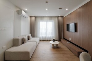 Una sala de estar moderna con un sofá, una mesa de centro, un televisor de pantalla plana montado en la pared y un amplio ventanal con cortinas.