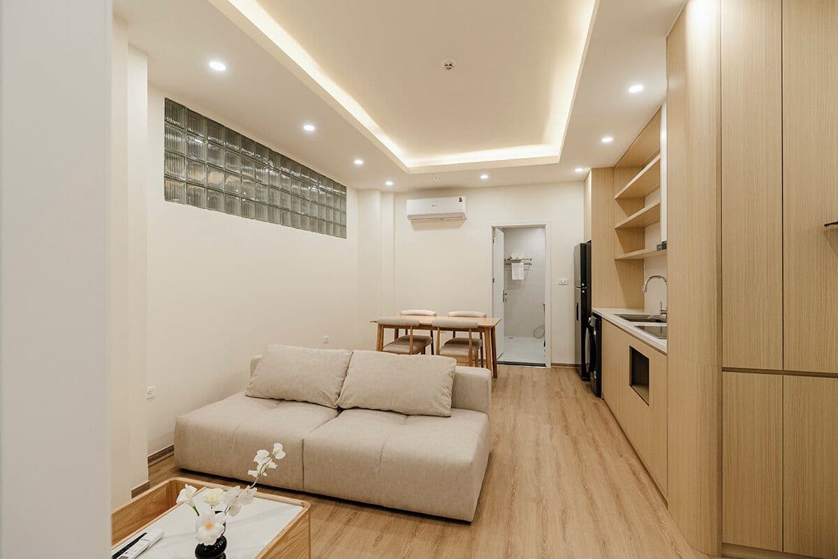 A compact living space with a sofa, dining table, kitchenette, and a glass block wall.