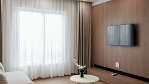 Une chambre d’hôtel moderne dotée d’une grande fenêtre, d’un téléviseur à écran plat fixé au mur, d’une table ronde agrémentée d’un vase de fleurs et d’un canapé.