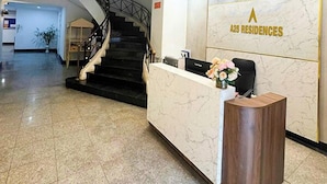 Un hall d’hôtel avec un comptoir de réception en marbre, un escalier et une enseigne murale indiquant « 25 Residences ».
