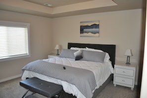 A bedroom with a bed, bedside tables, a bench, a painting, and a window with blinds.