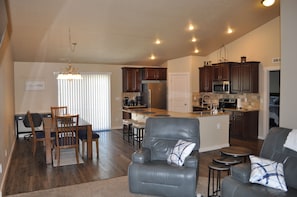 A spacious living area with a dining table, a leather sofa, and a kitchen with wooden cabinets and a built-in island.