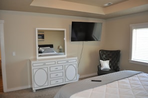 A bedroom with a bed, a dresser, a chair, a television, and a window.