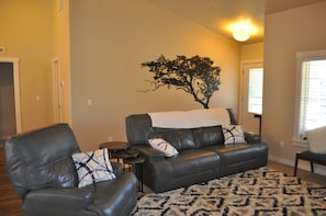 A living room with a sofa, two armchairs, a small table, and a decorative tree wall art piece.