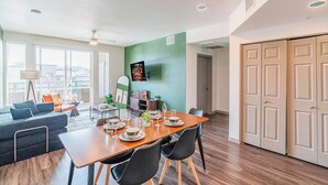 A modern living room with a dining area, a sofa, a coffee table, and a TV mounted on the wall. - Westgate Area Balcony, Pool, Gym Parking WD (Glendale)