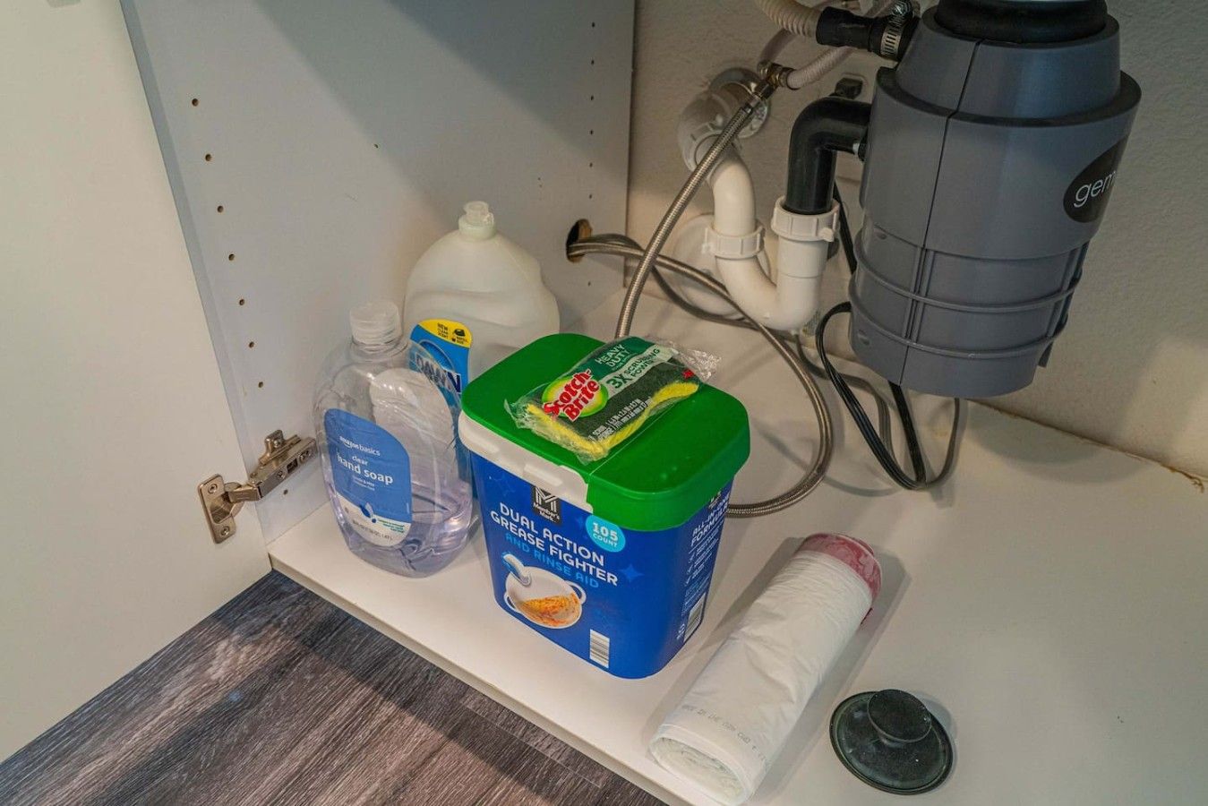 A bathroom shelf with a bottle of hand soap, a container of dual-action grease and grime remover, and a roll of toilet paper.