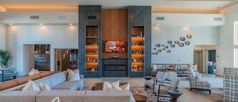 A spacious living area with a large sofa, a coffee table, and a fireplace. There are bookshelves and decorative items on the walls.