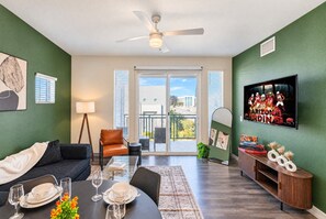 A living room with a sofa, dining table, and chairs, a ceiling fan, a TV mounted on the wall, and a balcony with a view of the city. - Modern Retreat | Stadium | Pool | Gym | W/D | PKG (Glendale)