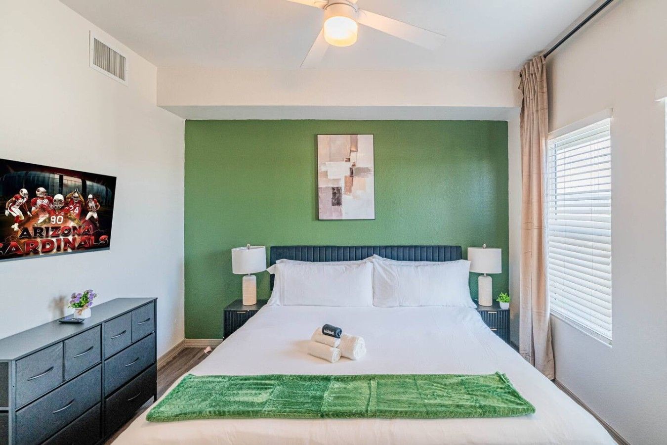 A hotel room with a bed, nightstands, a green wall, a ceiling fan, and a window with curtains.