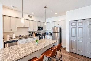 A modern kitchen with granite countertops, stainless steel appliances, and a central island with bar stools. - Modern Retreat | Stadium | Pool | Gym | W/D | PKG (Glendale)