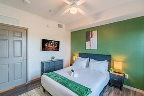 Une chambre d’hôtel comprenant un lit, une table de chevet avec une lampe, une commode, un ventilateur de plafond et une porte.