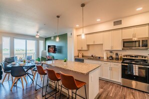 A modern kitchen with a central island, bar stools, a dining area with a table and chairs, and a large window providing a view. - Westgate Near Stadium Balcony Pool Parking Gym WD (Glendale)