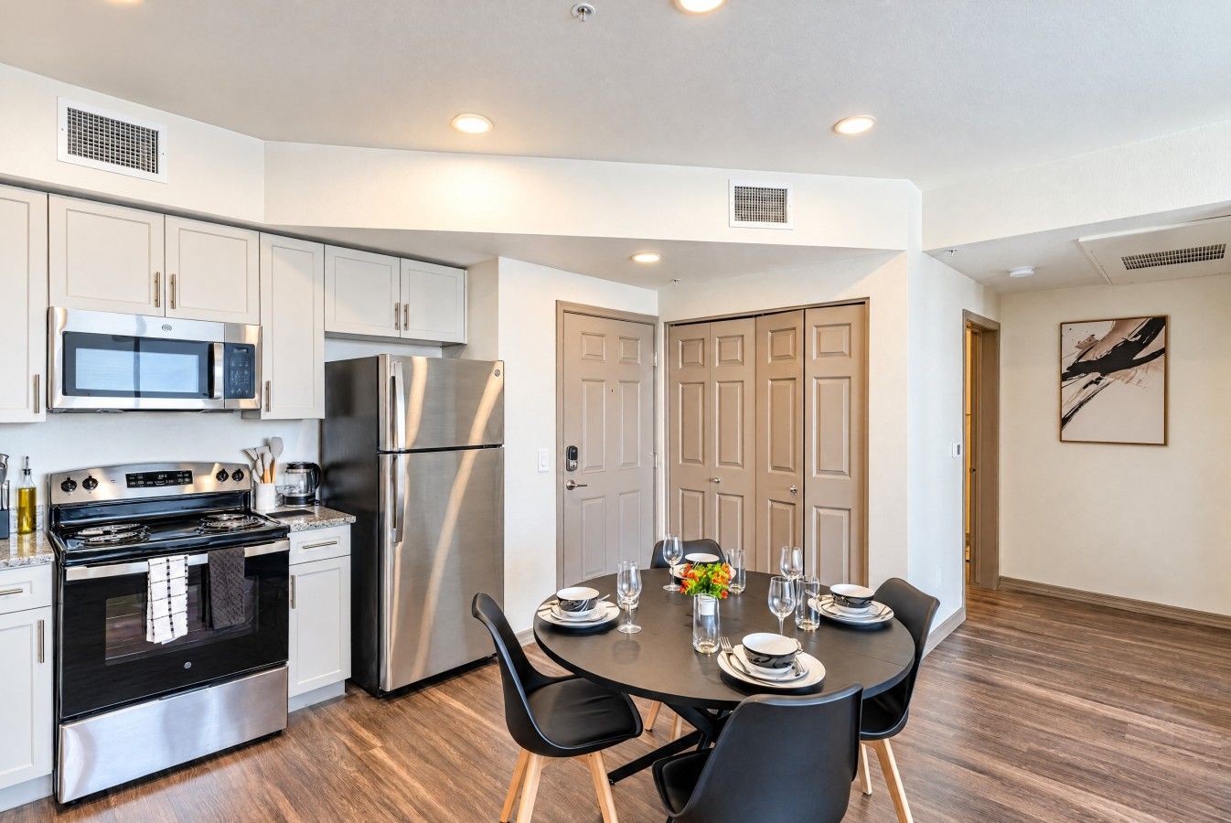 A modern kitchen with stainless steel appliances, a dining table set for four, and a wooden floor.