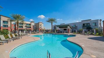 A swimming pool with lounge chairs and a covered area, surrounded by modern buildings.