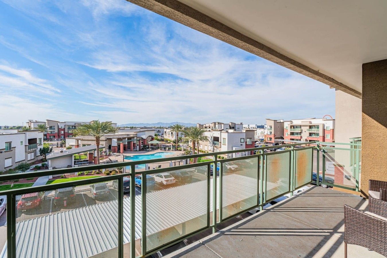 A balcony with a view of a swimming pool, adjacent buildings, and a clear sky.