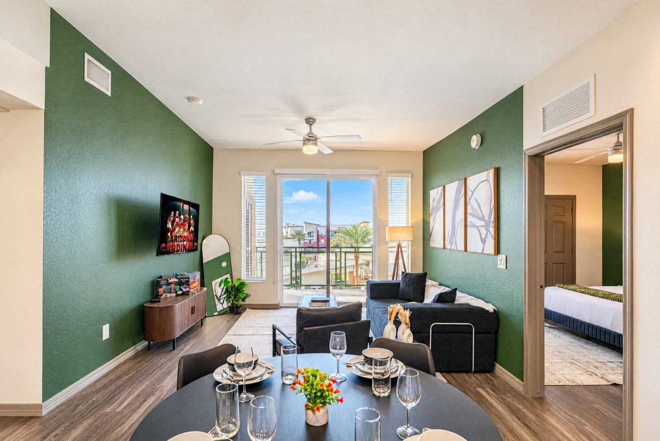 A dining area with a round table set for four, a ceiling fan, and a view of the outdoors through large windows.